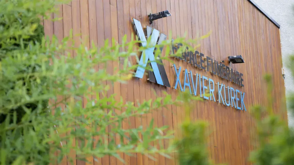 Enseigne de l'Espace Funéraire Xavier Kurek sur une façade en bois.