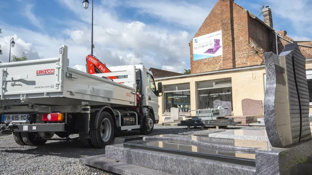 Camion de marbrerie et stèles en granit exposées devant l'entreprise.